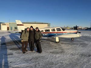 three women stand in front of a small plane
